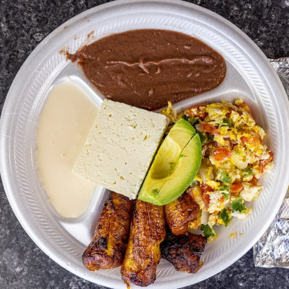 Honduran breakfast with refried beans, plantains, cheese, avocado, and scrambled eggs on a divided plate.