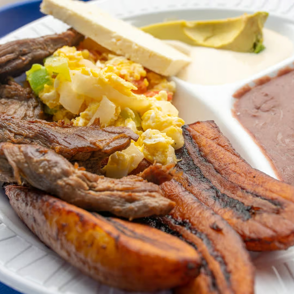 Honduran breakfast with steak, scrambled eggs, fried plantains, refried beans, cheese, and avocado.