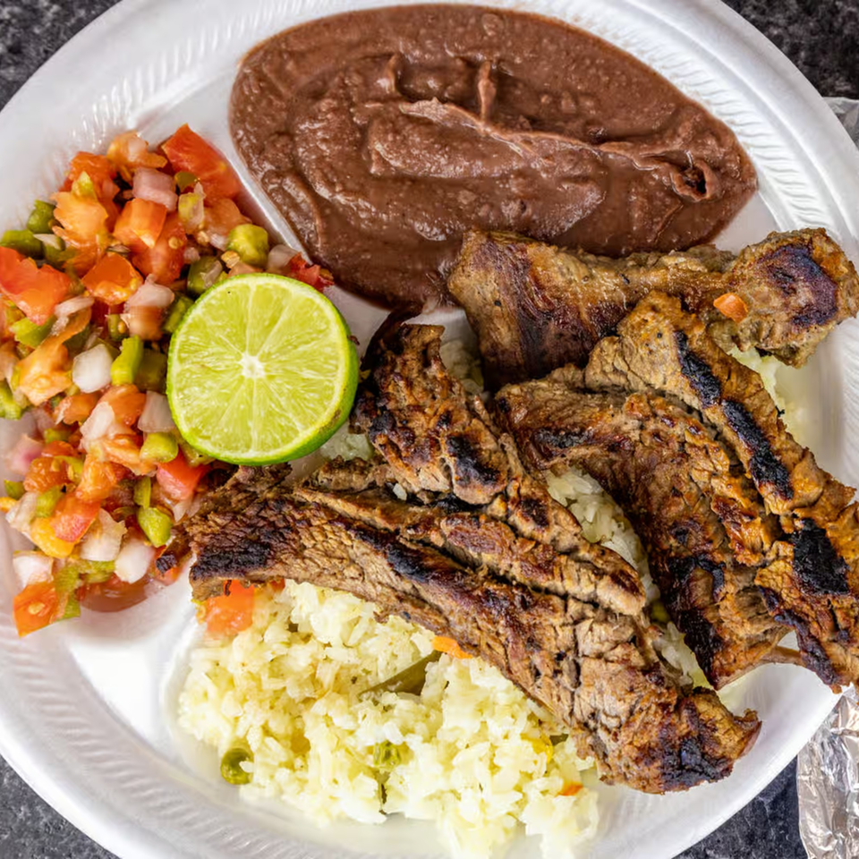 Honduran grilled steak with rice, refried beans, pico de gallo, and a lime wedge on a white plate.
