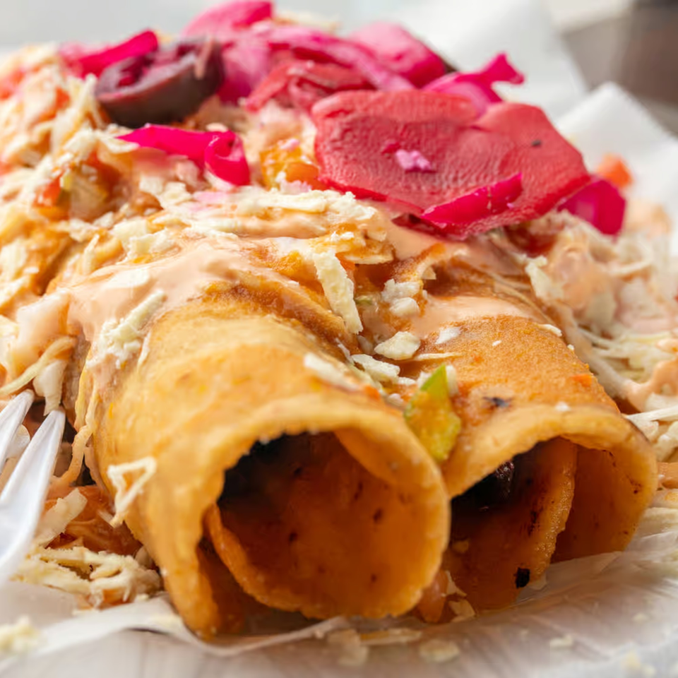 Two Honduran taquitos with shredded cabbage, pink pickled onions, and creamy sauce.