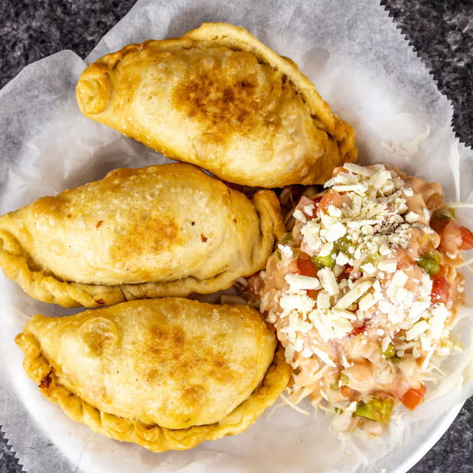 Three golden-fried Honduran empanadas with a side of cabbage salad topped with cheese and dressing.